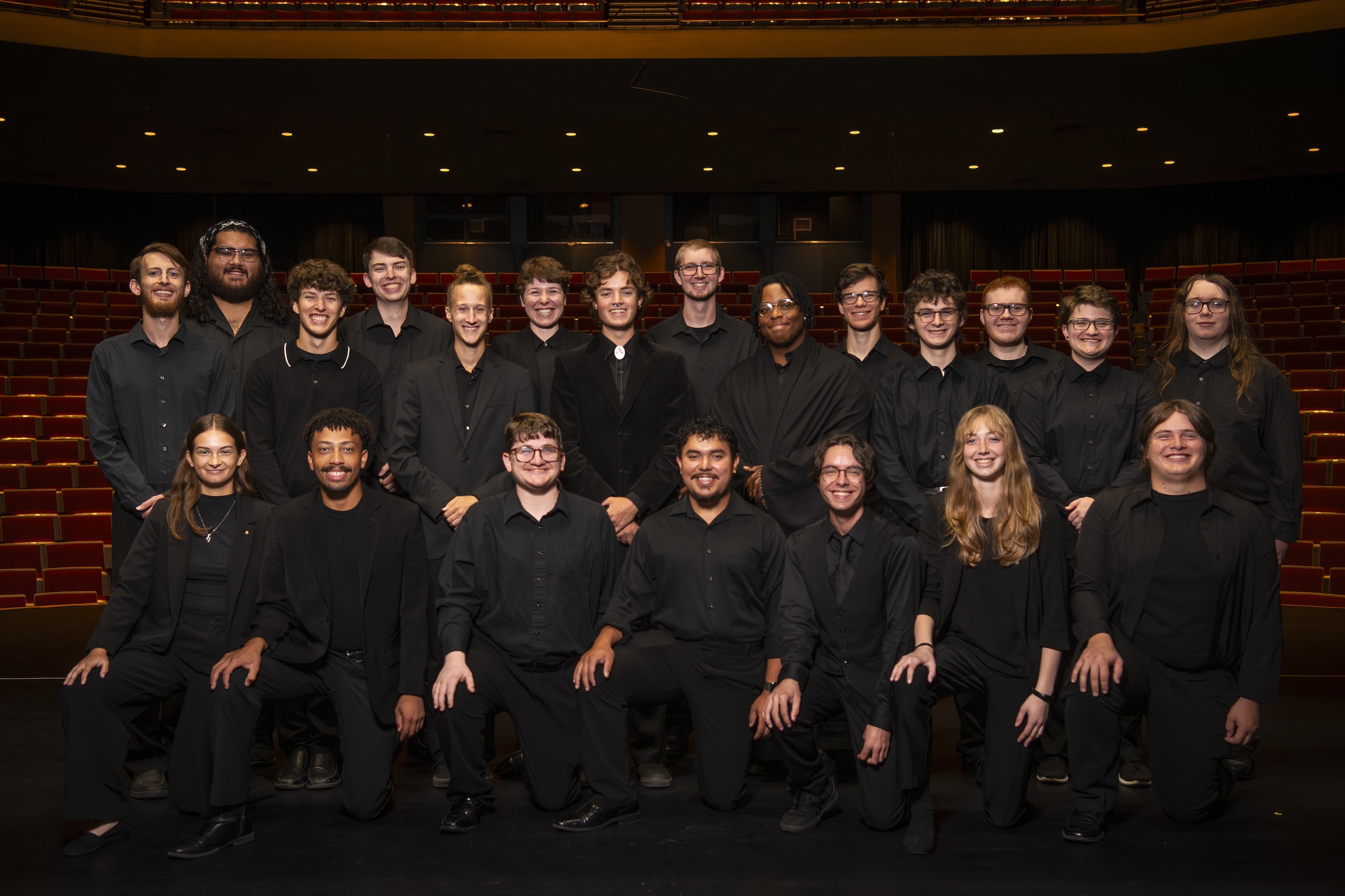 2025-2026 Percussion Studio Two rows of students dressed in black stand with the seating of a concert hall behind them.