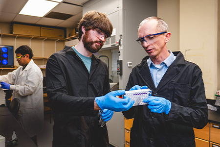 Nicholas Wallace, right, studies HPV’s role in causing cancer. Graduate students Abhineet Banerjee, far left, and Grant Brooke, center, assist in his research lab.
