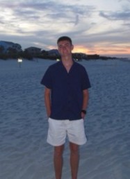 A young man standing on the beach at sunset.