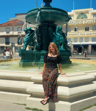 A young woman sitting on the edge of a fountain.