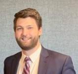 Professional headshot of Josh Wilson wearing a grey suit and maroon tie.