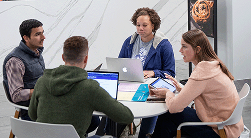 a group of 4 students sit around a table, working on a project