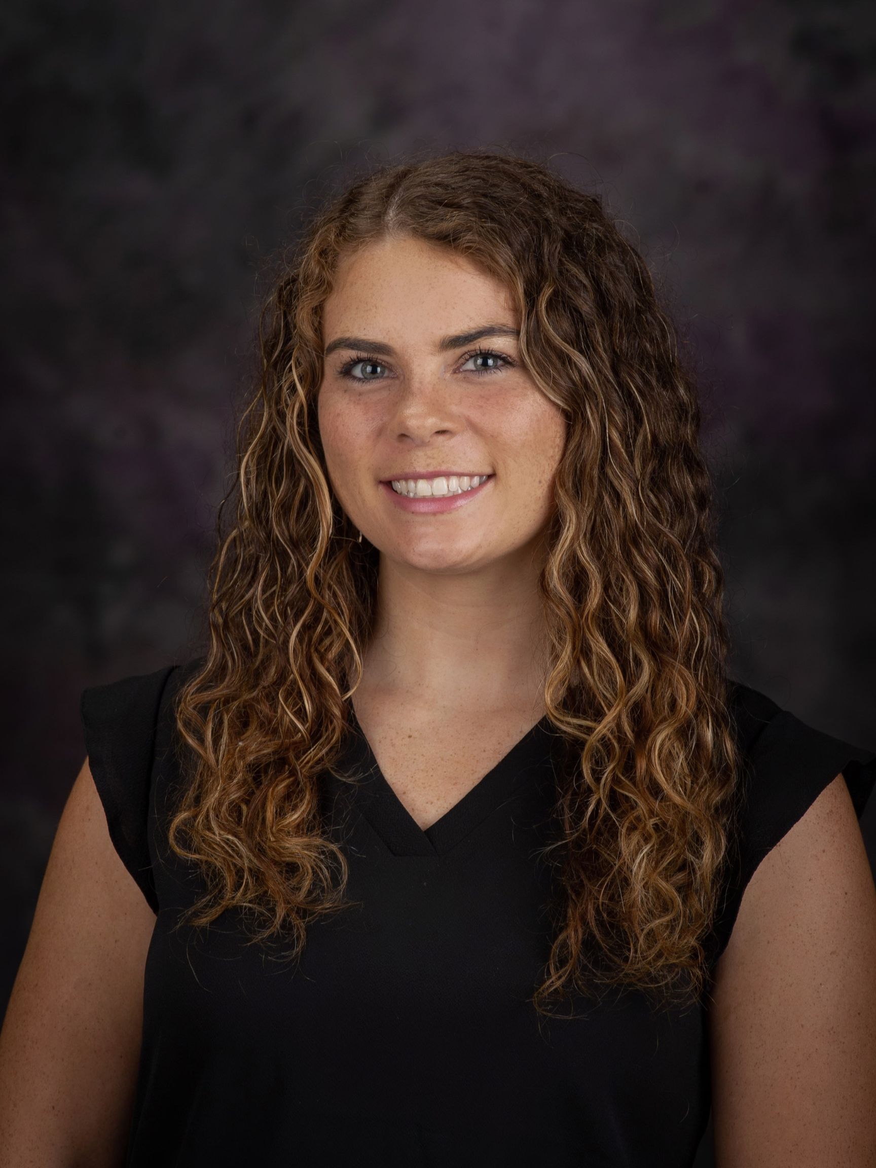 Professional headshot of Kayleigh, a white woman with curly light brown hair wearing a black top.
