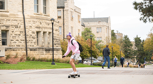 A K-Stater longboards past Hale Library.