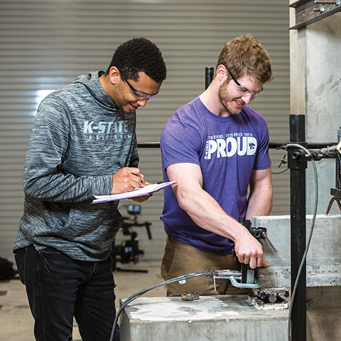 Two engineering students work together to test a piece of cement in a studio classroom setting.