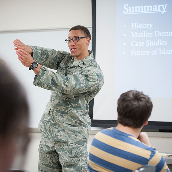 A student in Army fatigues gives a presentation in a political science classroom to his peers.