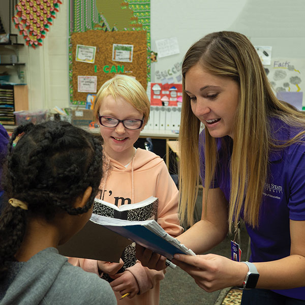 An education student looks over an assignment with two young elementary school-aged students.