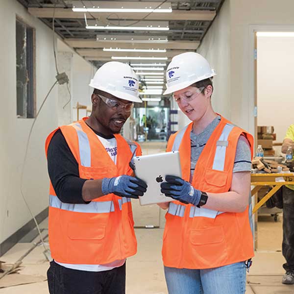 Two engineering students review a plan on a tablet in a construction setting.
