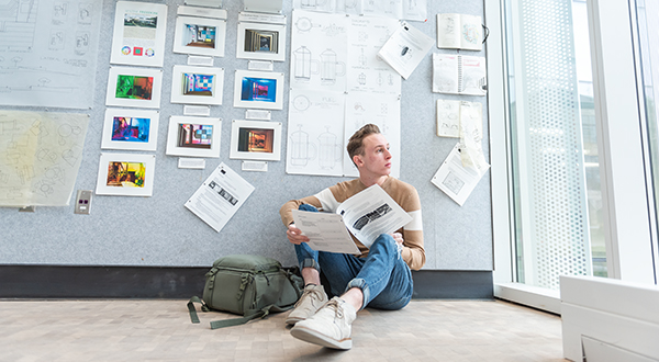 man staring out window with plans on the wall