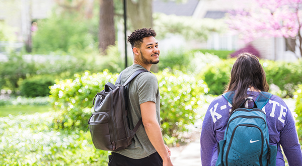 a student wearing a backpack looks back at the camera while walking with a classmate looking at the path ahead