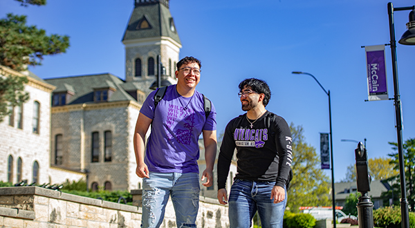 two students walking towards fairchild with anderson hall behind them