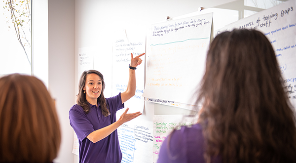 a woman showing two coworkers a white sheet of paper with business ideas written on it