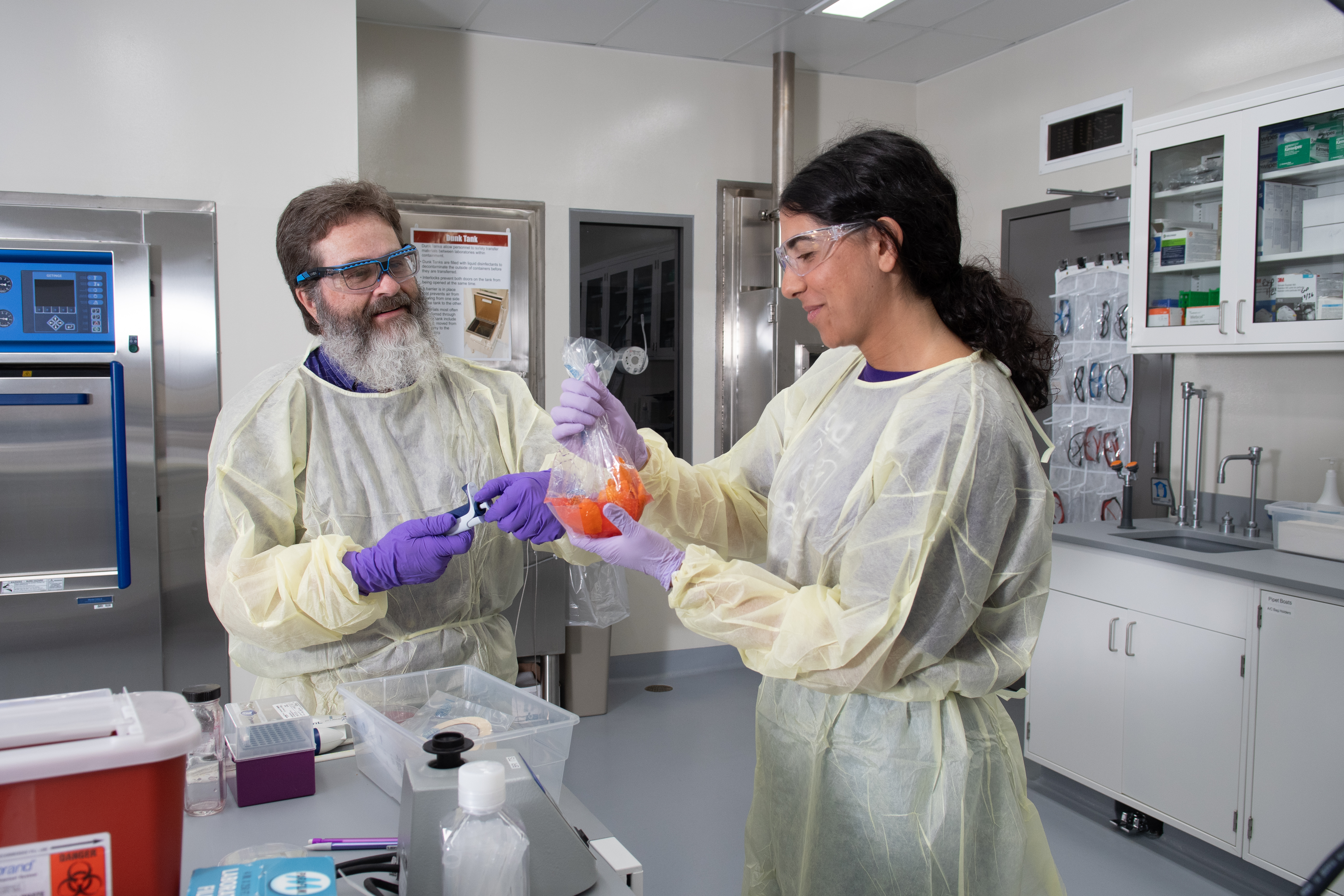 Professor Randy Phebus is preparing a chicken nugget for experimentation within a food science lab. He is wearing a pale yellow disposable isolation gown, purple rubber gloves and safety glasses.