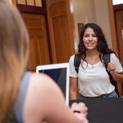 Student walking into an area with a woman behind a desk with a tablet.