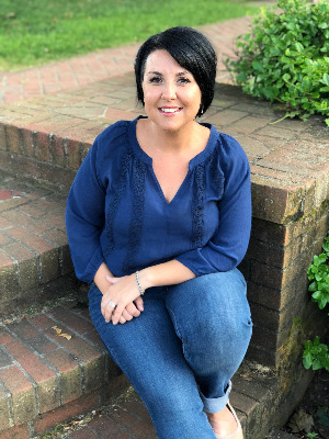 Image of Brooke sitting on brick stairs wearing a blue blouse and jeans