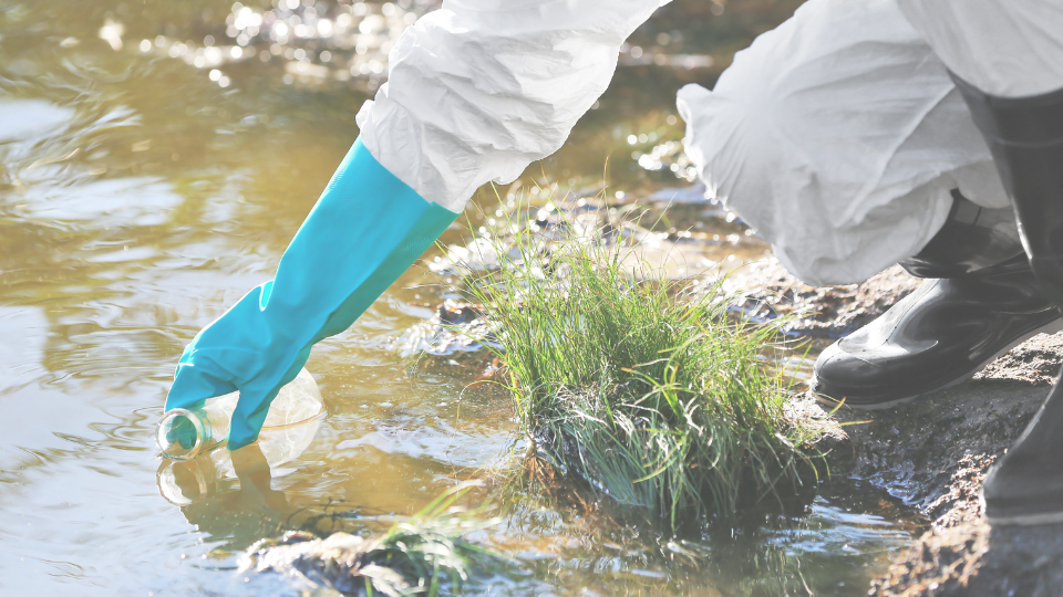 Person wearing PPE collecting a water sample ourdoors