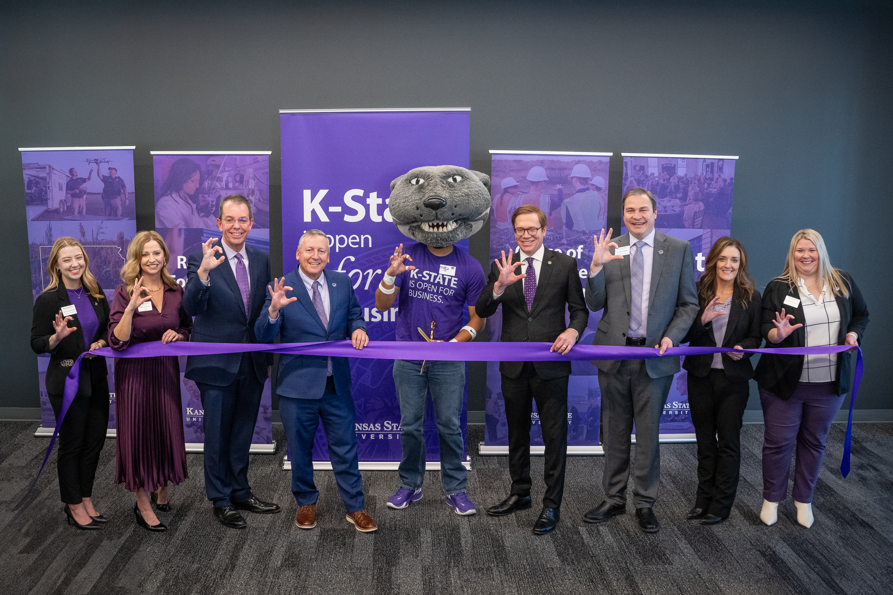 Eight people and Willie Wildcat stand behind a ribbon before the ribbon cutting event.
