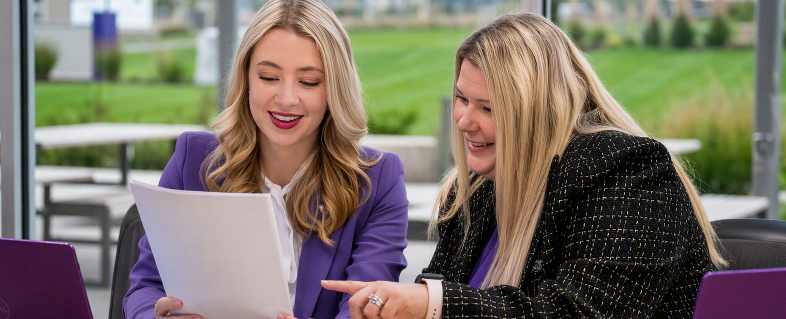 Two women sit at a conference table and look at a piece of paper.