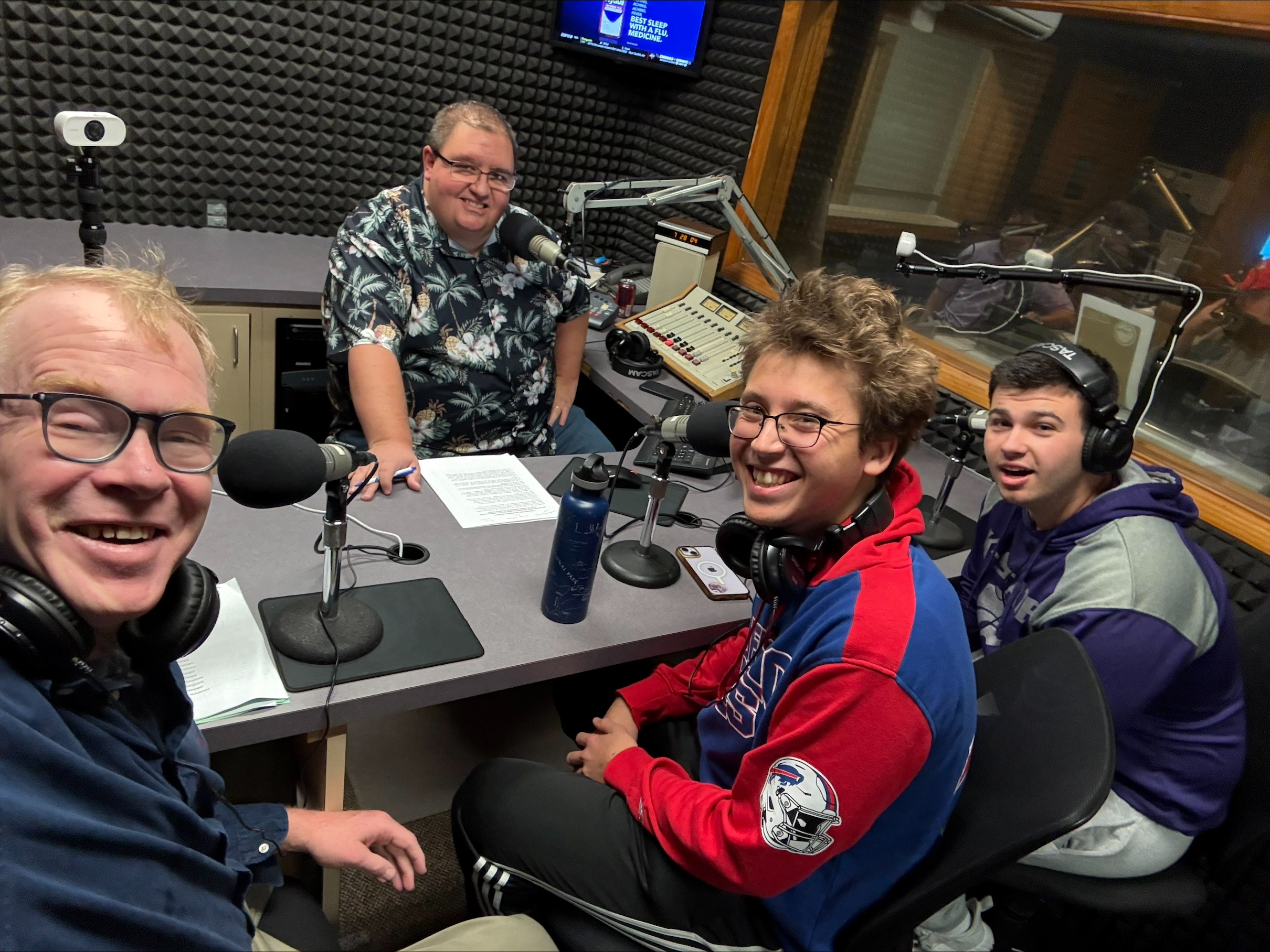 Four men inside of a radio booth looking at the camera with smiles