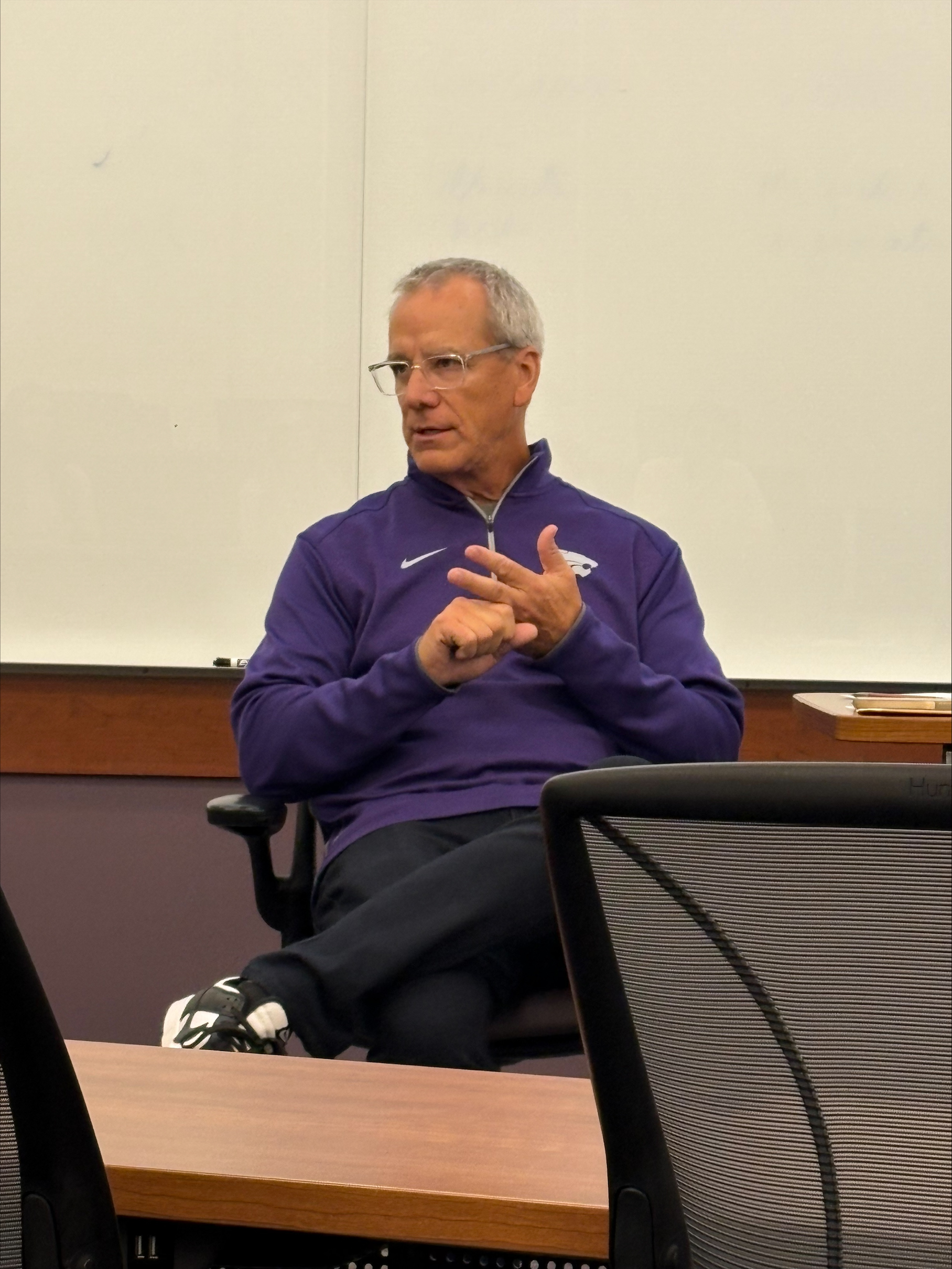 Man sitting in a chair with glasses wearing a K-State pullover