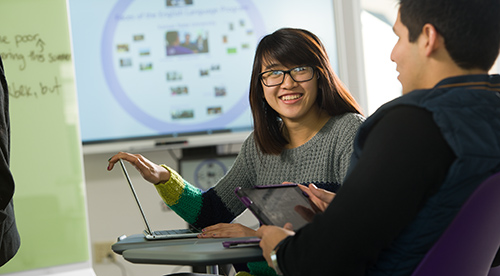 A student with a laptop talking to another student