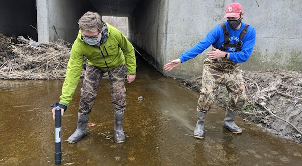 Two researchers take water quality samples in a waterway