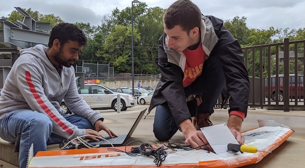two students work on the equipment attached to a small aircraft