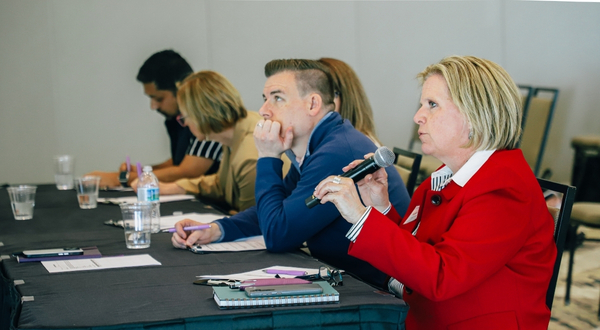 adults sit attentively at a table to listen to presentations