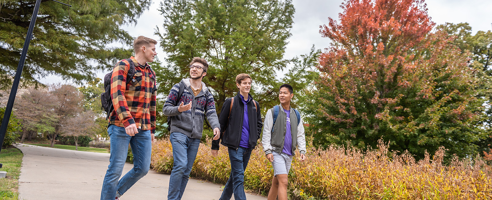 Four students in jackets and backpacks talk and laugh together while walking past Beach Art Museum