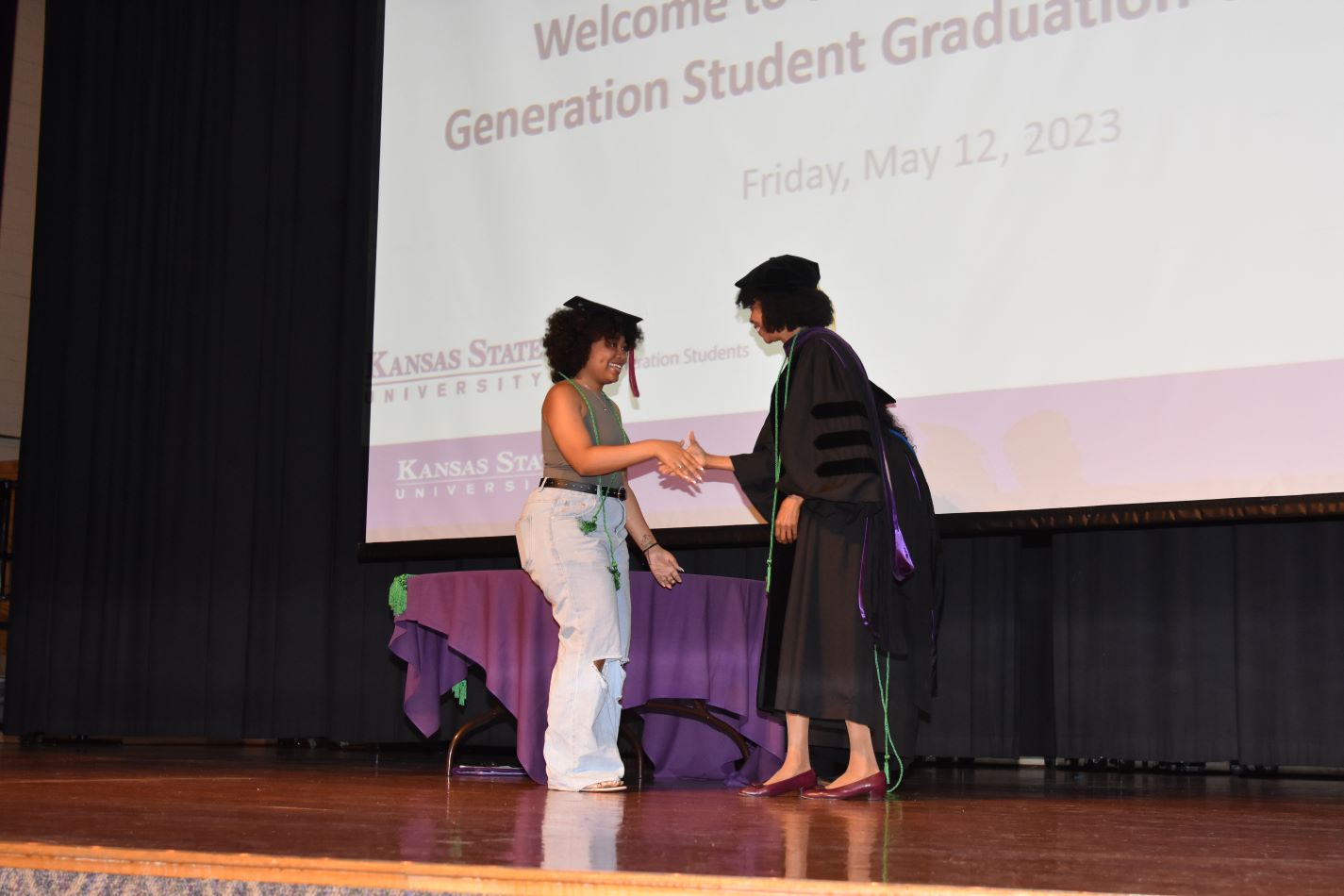 Dr. Rana Johnson is shaking a student's hand on stage during the 2023 graduation celebration.