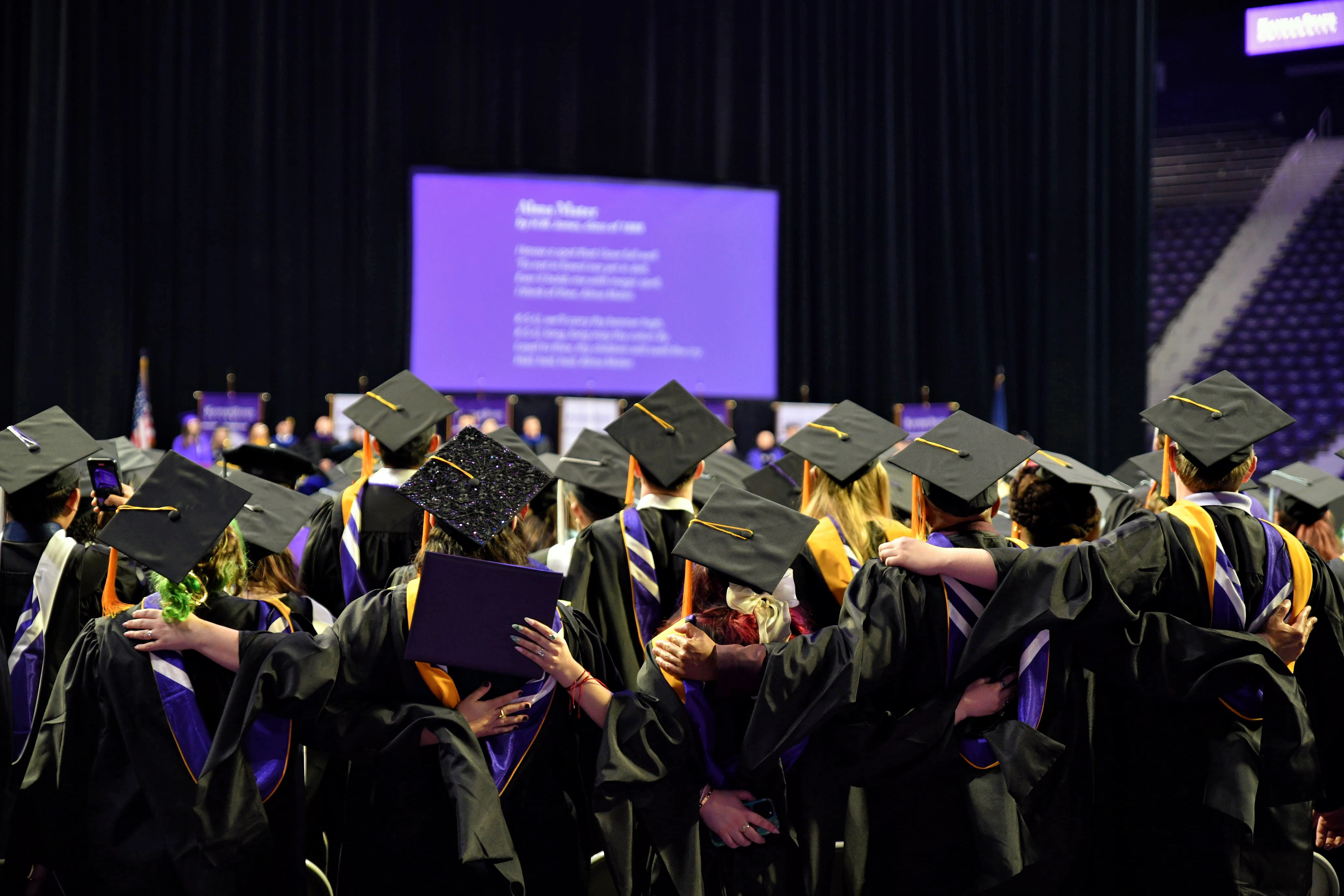 Graduates facing the screen with their arms around each other 