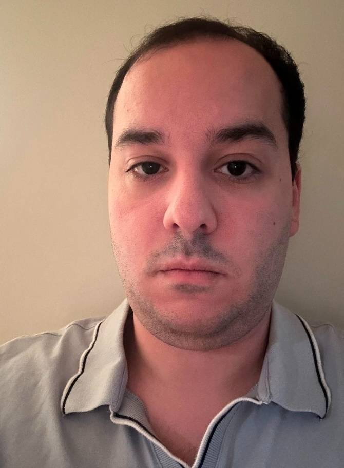 Photo of white man with short brown hair standing in front of a bare wall.