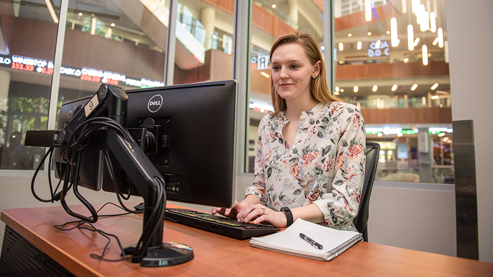 a woman looking at a computer monitor with a notebook beside her