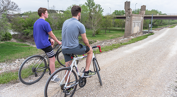 two cyclists stopping on a gravel trail to take in a bridge view