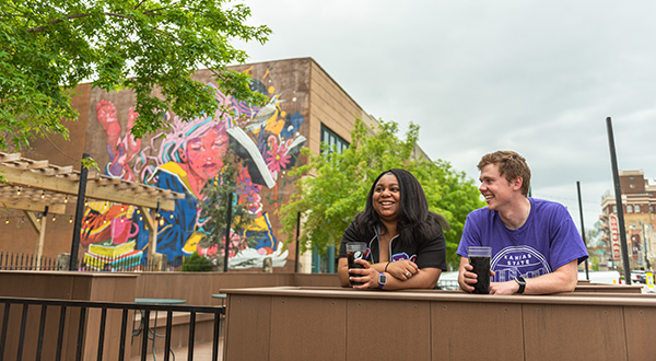 a man and woman seated in front of a mural smiling