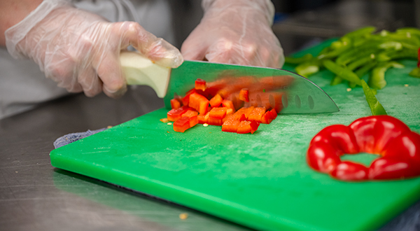 a knife cutting orange peppers and produce