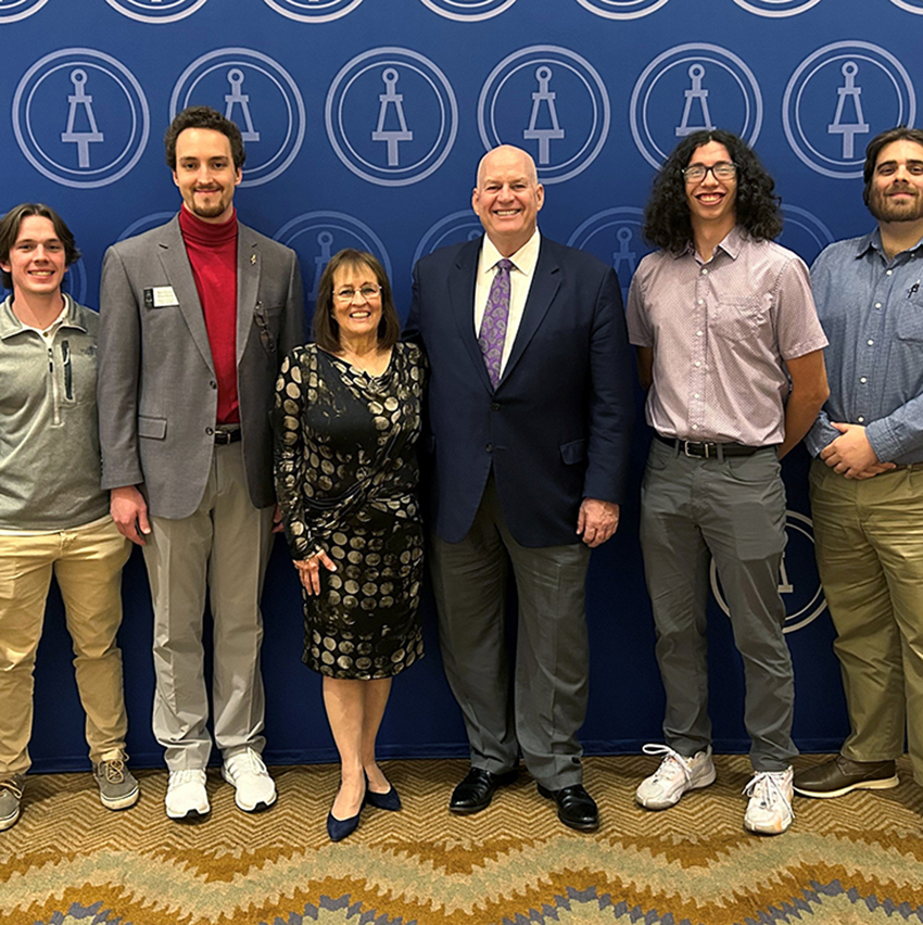 A group of college student and faculty pose in a line for a group photo.