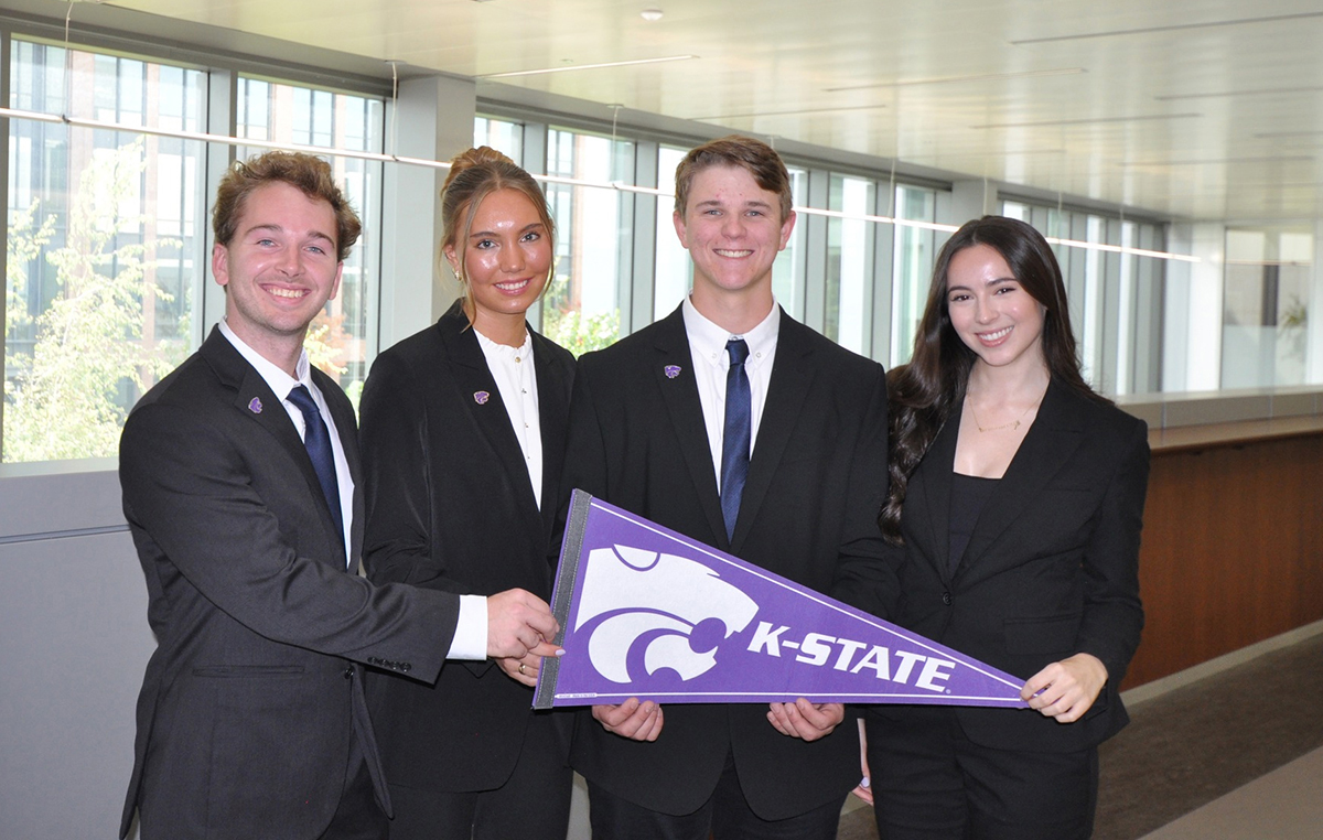 Four college students in business attire smile for a group photo with a purple K-State pendant. 