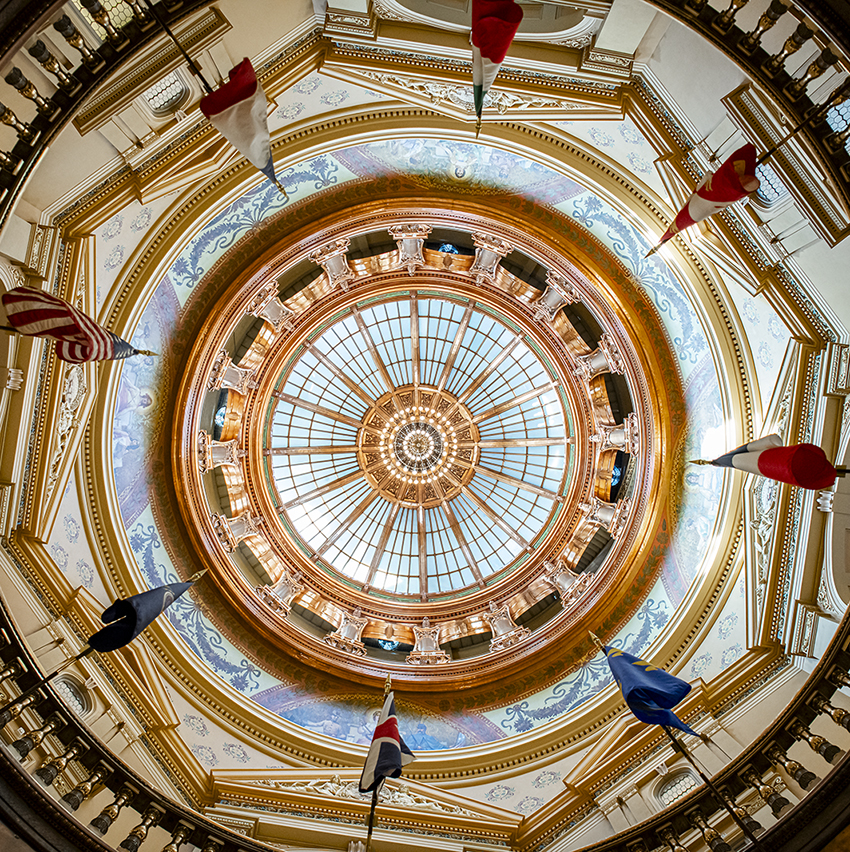 An underneath view shows the circular and brightly lit roof of the Kansas Capitol rotunda.