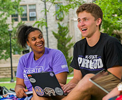 Two students in Proud shirts on the grass in the Quad.