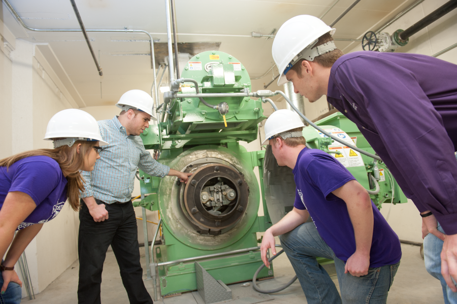 Students and faculty wearing hardhats inspect a feed mill