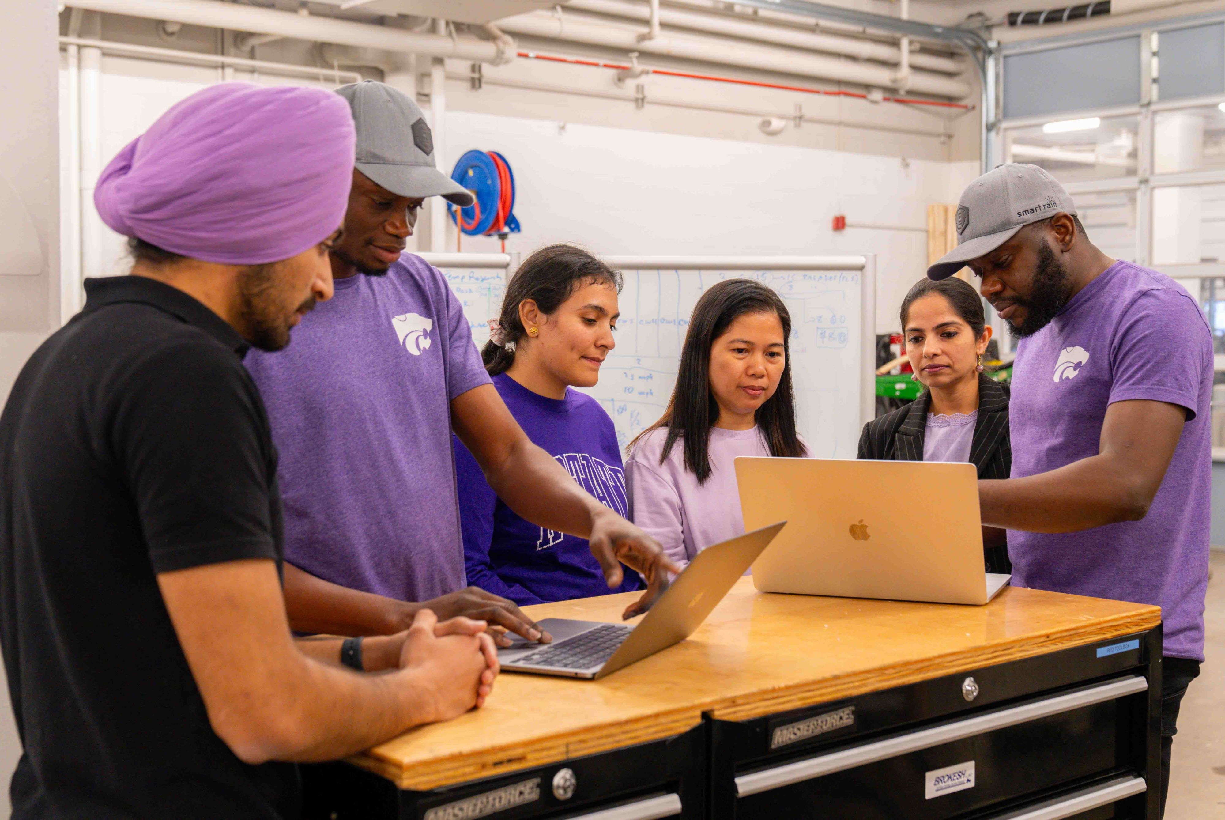 A group of students and mentors collaborate at a workstation.