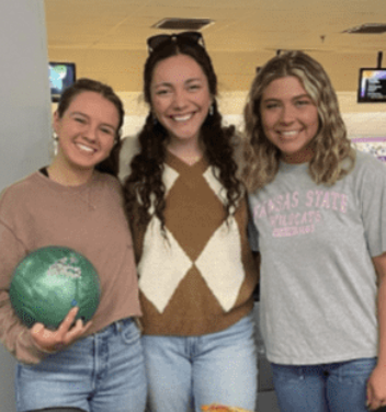 Three female students smiling, one holding a green bowling ball
