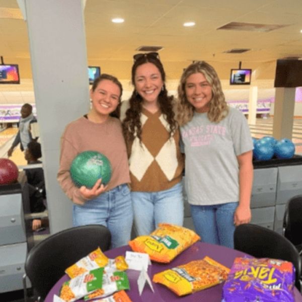 Three female students smiling, one holding a green bowling ball