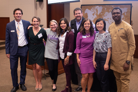 Group of doctoral students and faculty smiling at podium