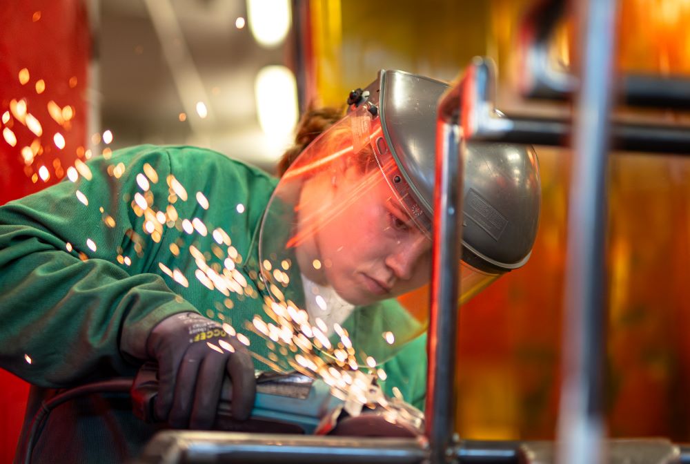 A student uses a grinder tool to cut a piece of metal