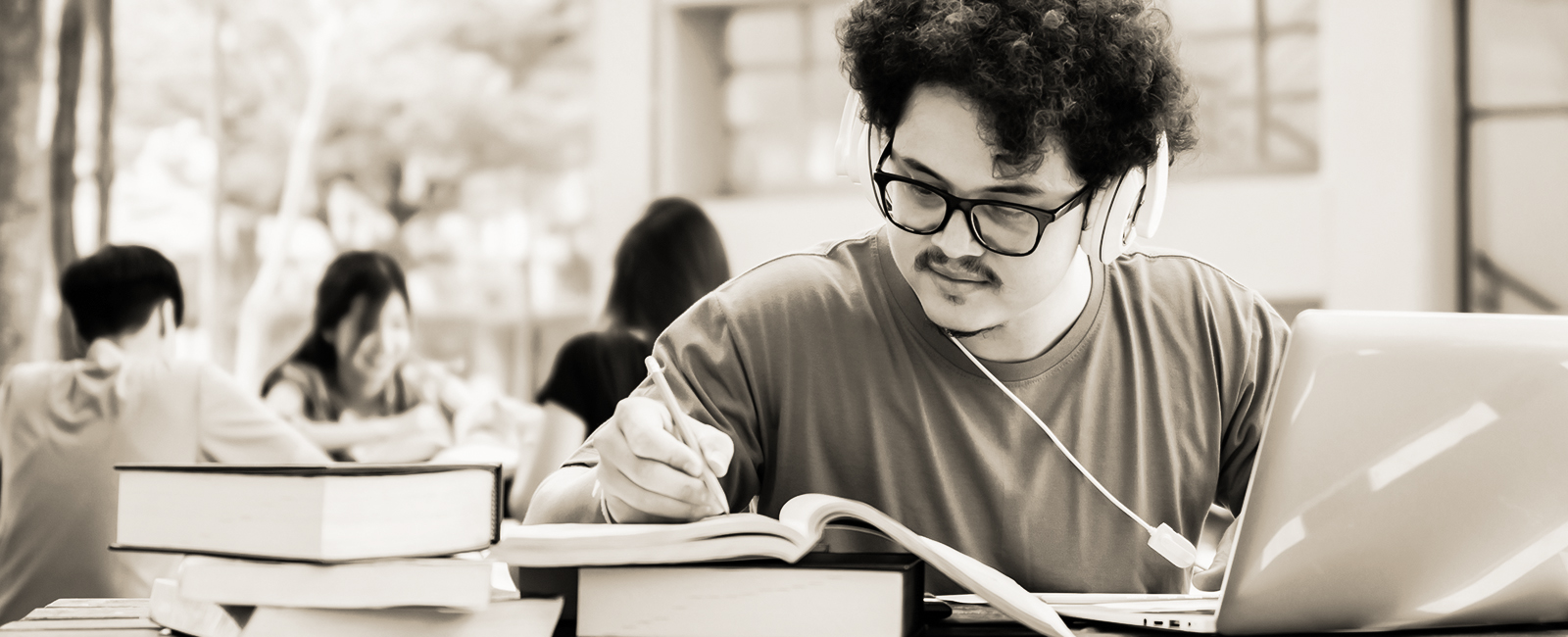 student in the library on a laptop and reading a textbook