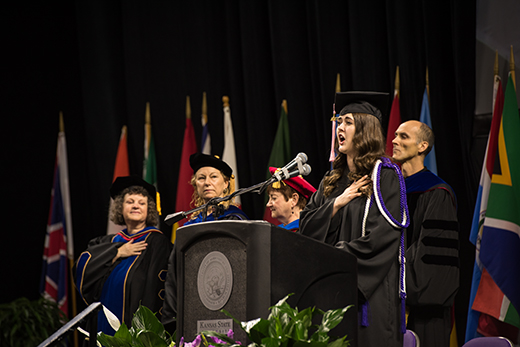 A candidate for graduation sings the national anthem at a Kansas State University commencement ceremony.