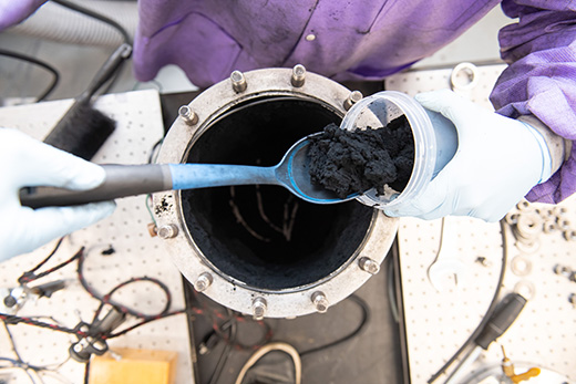 In this image, a researcher scoops out large quantities of graphene from a small detonation chamber.