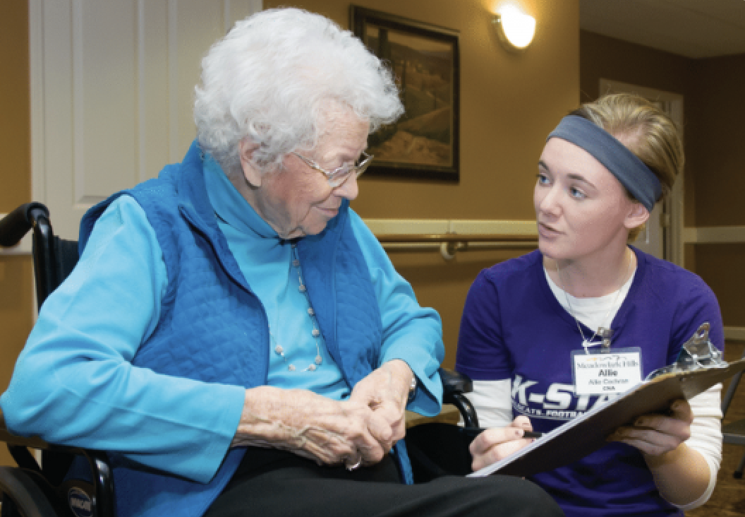 An older adult and a researcher with a clipboard discussing information